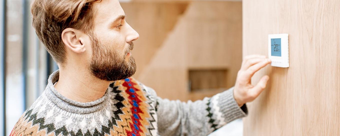 Man met een warme trui aan zet de thermostaat lager