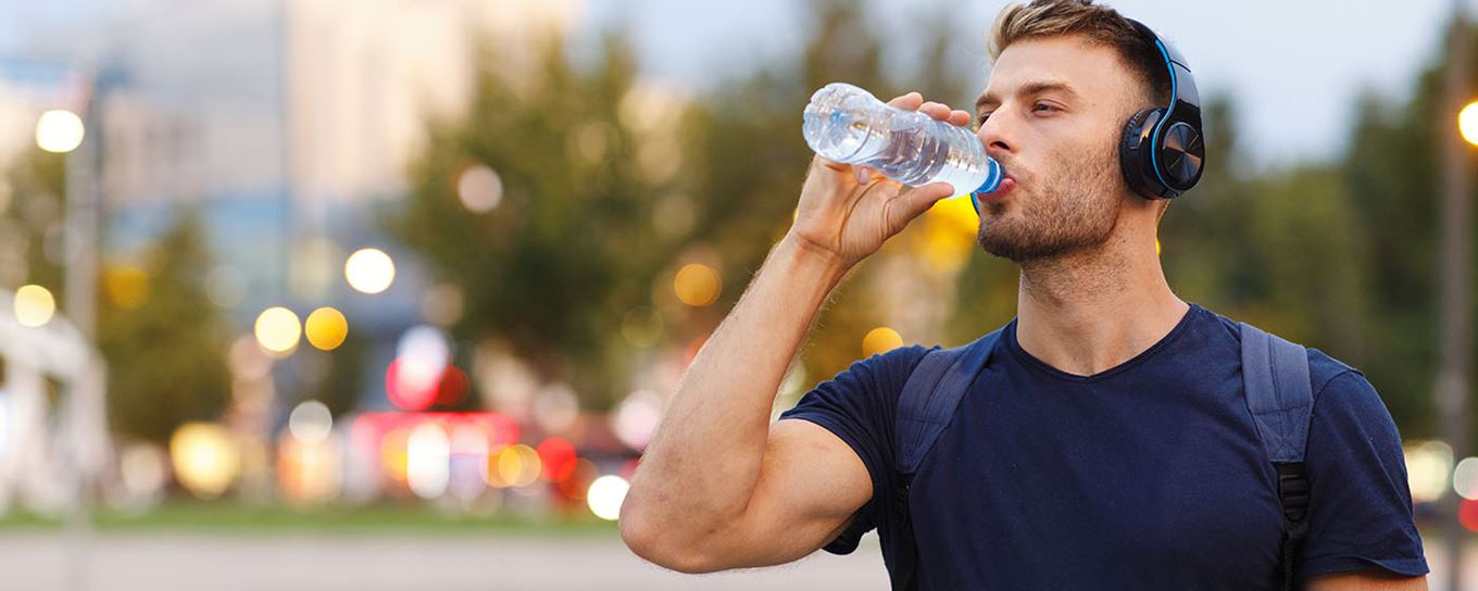 Jongeman met koptelefoon op drinkt water uit een flesje | a.s.r.