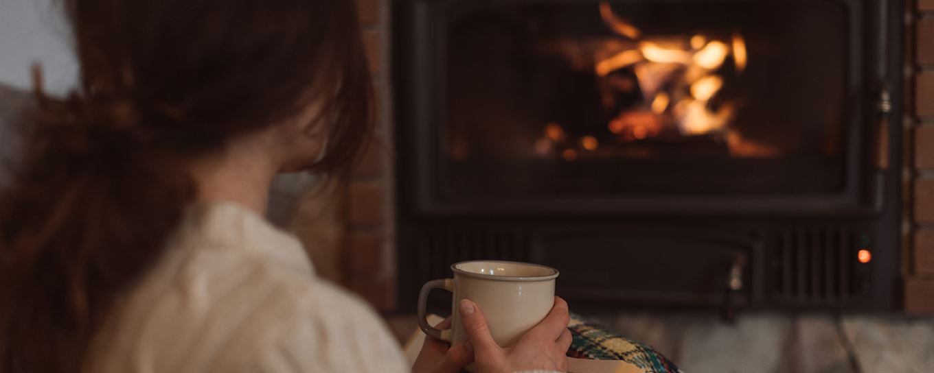 Vrouw met mok in de hand zit voor het haardvuur | voorkomen schoorsteenbrand | a.s.r.