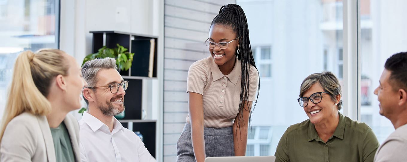 Vrouw staat en kijkt lachend naar vier andere mensen die zitten