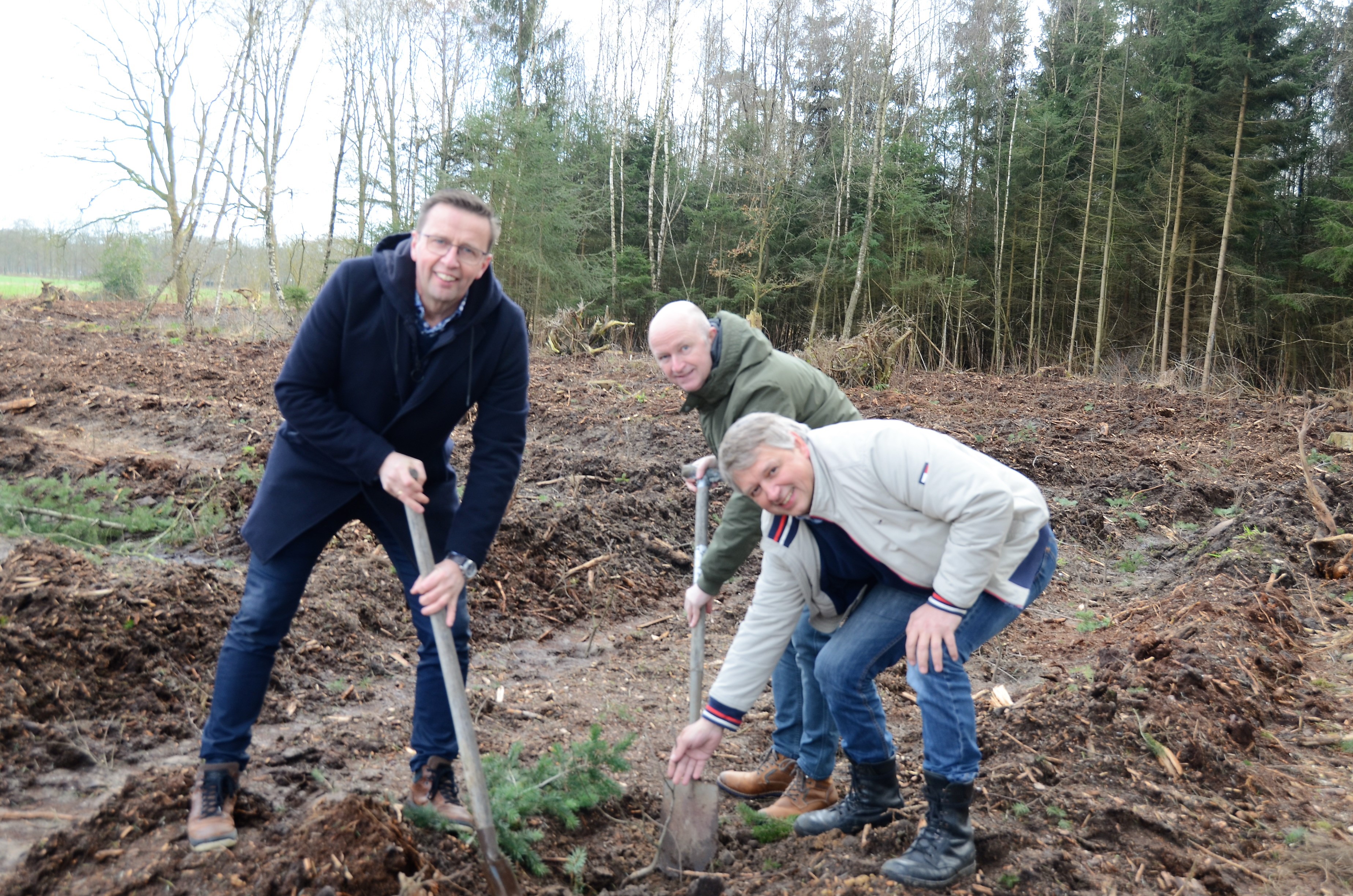 Drie mensen kijken lachend in de camera met een schep in de handen. Samen planten ze een boom