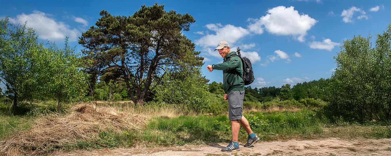 man die in de duinen aan het wandelen is al kijkend op zijn horloge om te stappen te tellen