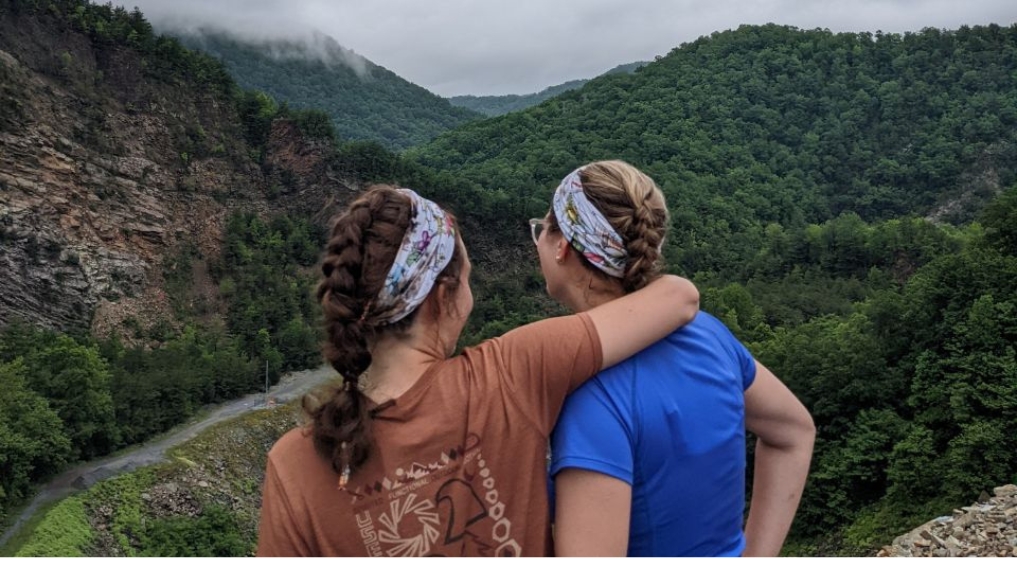 twee wandelvriendinnen arm over schouder staand op een berg