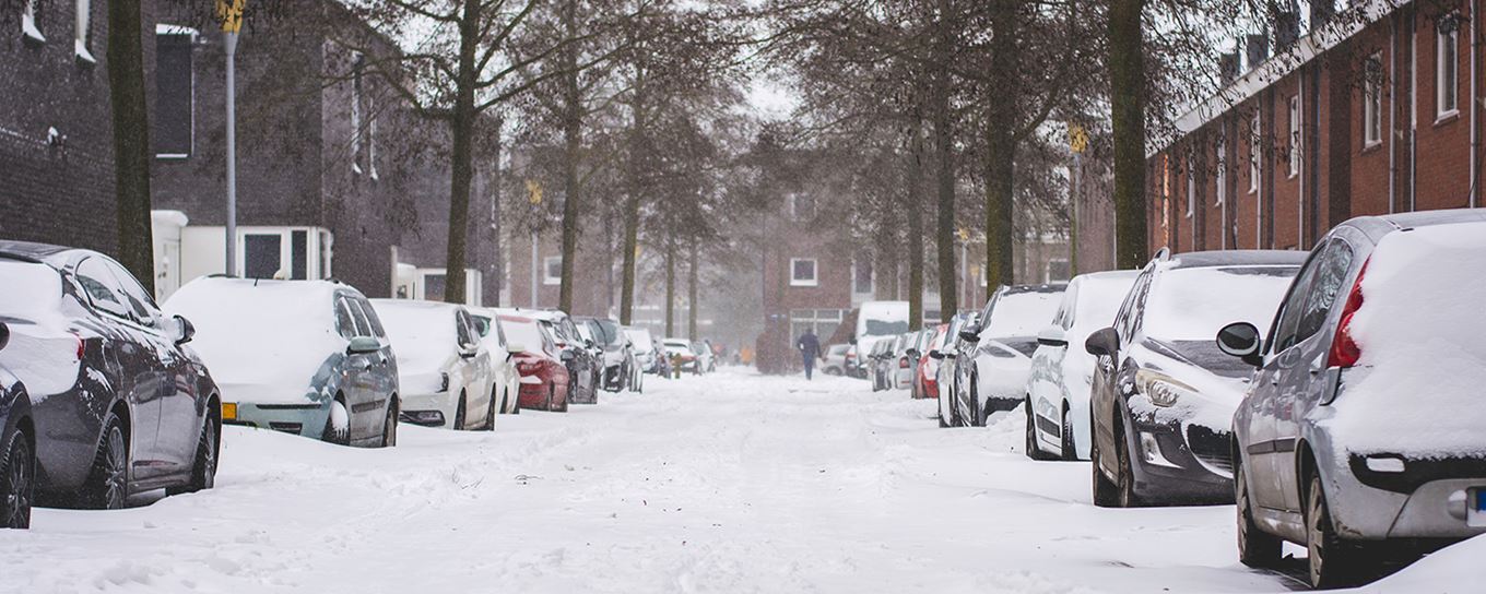 Een straat met geparkeerde auto's aan de zijkanten met overal een flink laag sneeuw