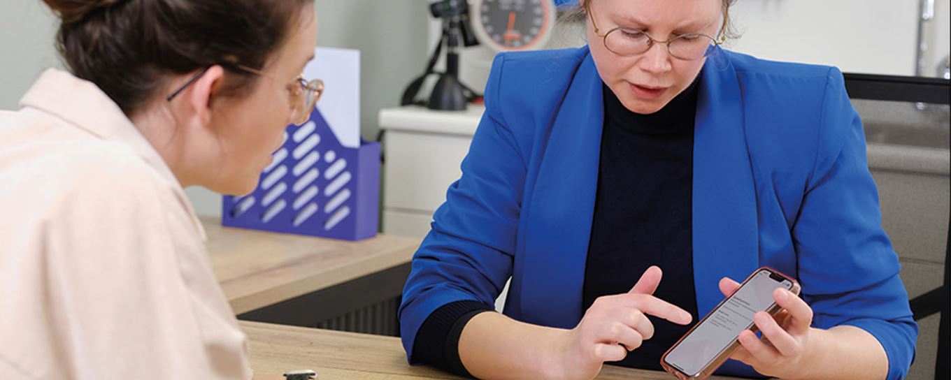 Afbeelding van een huisarts met een telefoon in haar handen en ze legt wat uit aan de patient