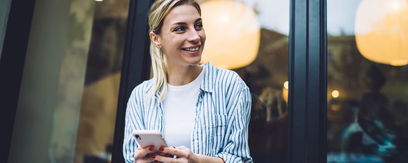 Een jonge vrouw lachend kijkend naar links met haar mobiel in haar handen