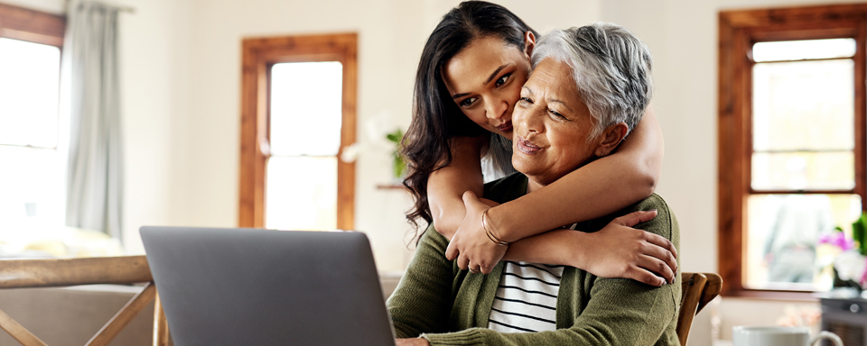 Een dochter omhelst haar moeder die achter een laptop zit