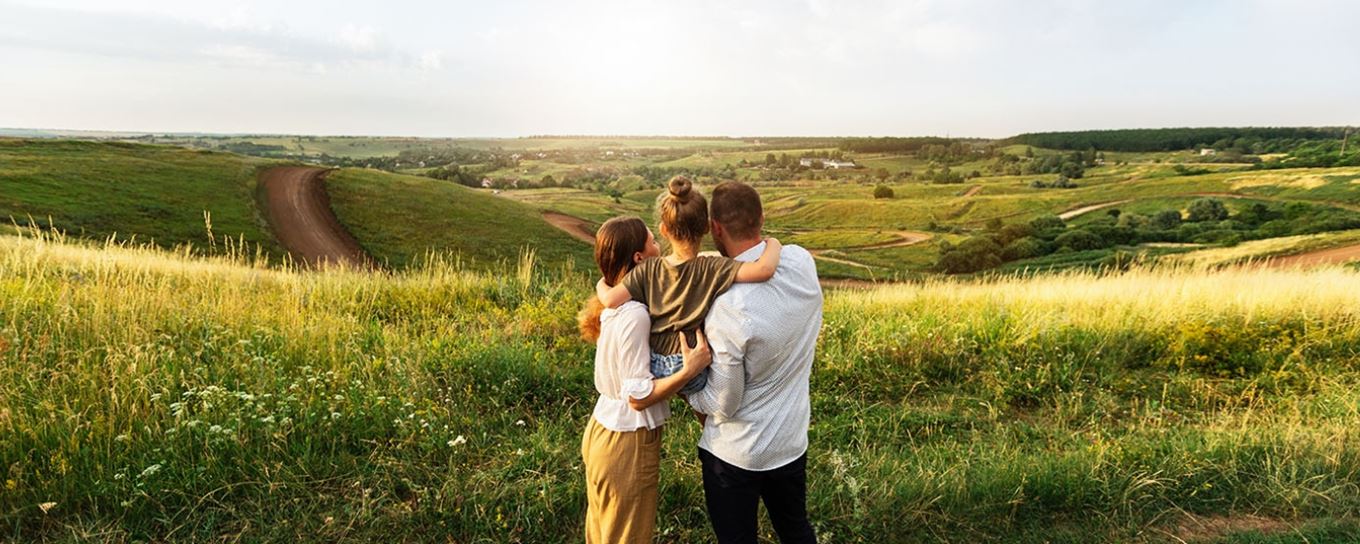 Een moeder, kind en vader knuffelend kijkend over de heuvels op hun vakantie