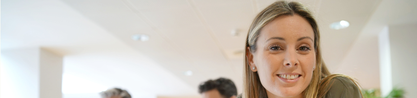 Vrolijke jonge vrouw kijkt in de camera met collega's op de achtergrond | Doenpensioen | a.s.r.