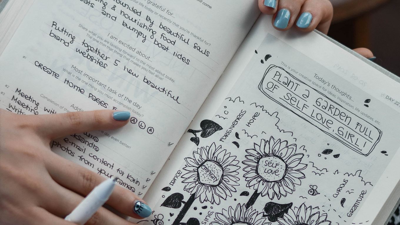 Op de foto zijn ahnden te zien en een bullet jorunal. In eht journal staan dingen als Plant a garden full of self love girl. Daaronder een vrolijke tekening met bloemen waarin staat: empathy, self love. 