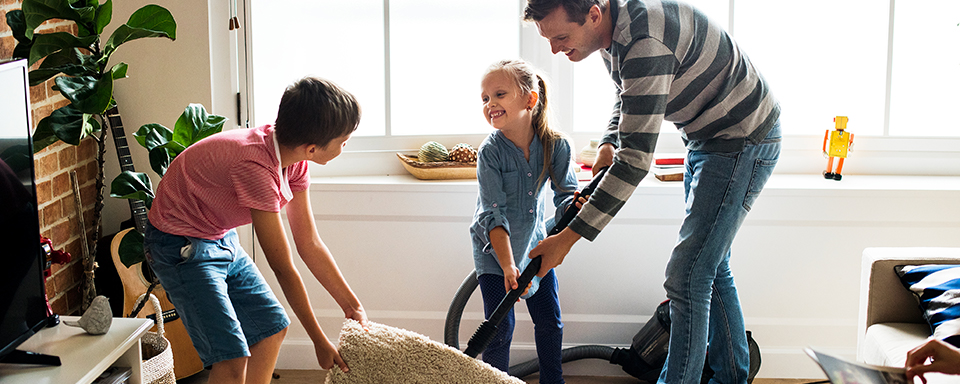 Man en twee kinderen stofzuigen samen woonkamer
